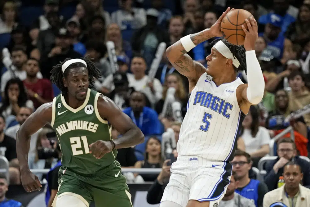 Orlando Magic's Paolo Banchero (5) looks to pass the ball as he is guarded by Milwaukee Bucks' Jrue Holiday (21) during the first half of an NBA basketball game, Monday, Dec. 5, 2022, in Orlando, Fla. (AP Photo/John Raoux)