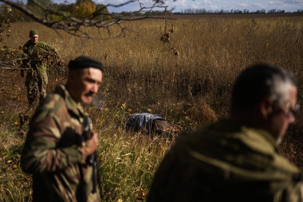 Efectivos de las fuerzas de defensa territorial de Ucrania encargados del desminado, junto al cuerpo de un residente que murió por la explosión de una bomba rusa, en Hrakove, Ucrania, el 13 de octubre de 2022. (AP Foto/Francisco Seco)
