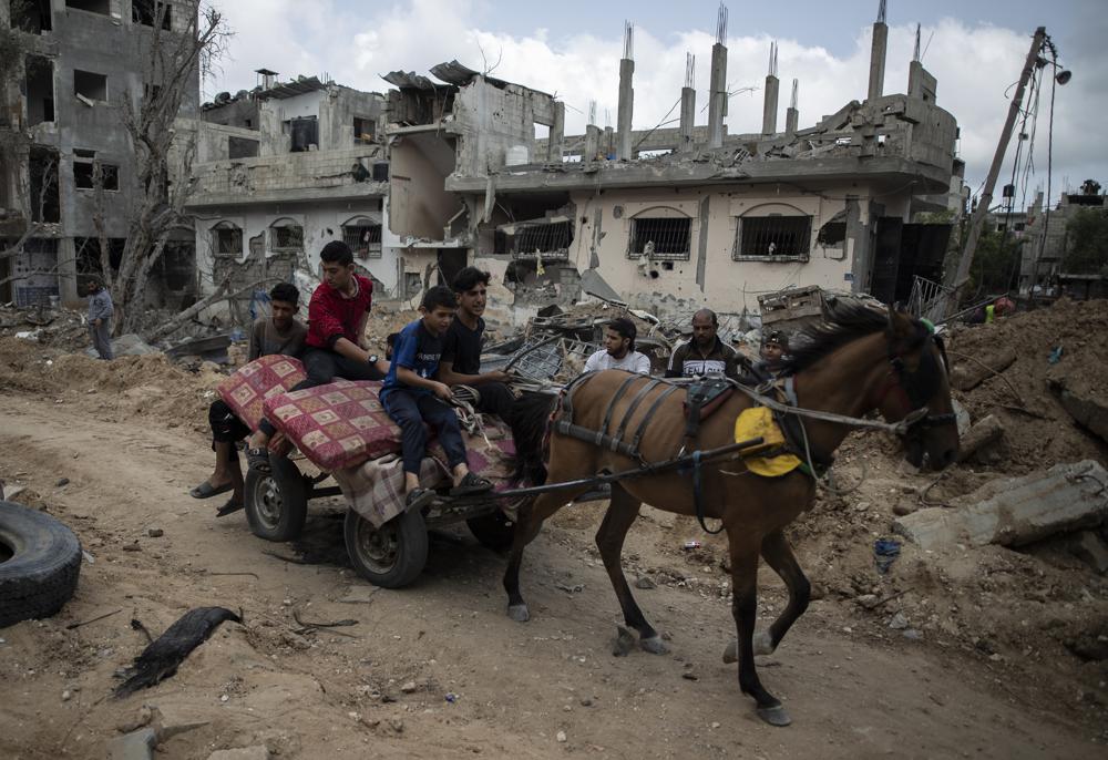 Palestinians on a horse carte loaded with belongings, pass by destroyed homes, to which they returned following a cease-fire reached after an 11-day war between Gaza's Hamas rulers and Israel, in town of Beit Hanoun, northern Gaza Strip, Friday, May 21, 2021. (AP Photo/Khalil Hamra)