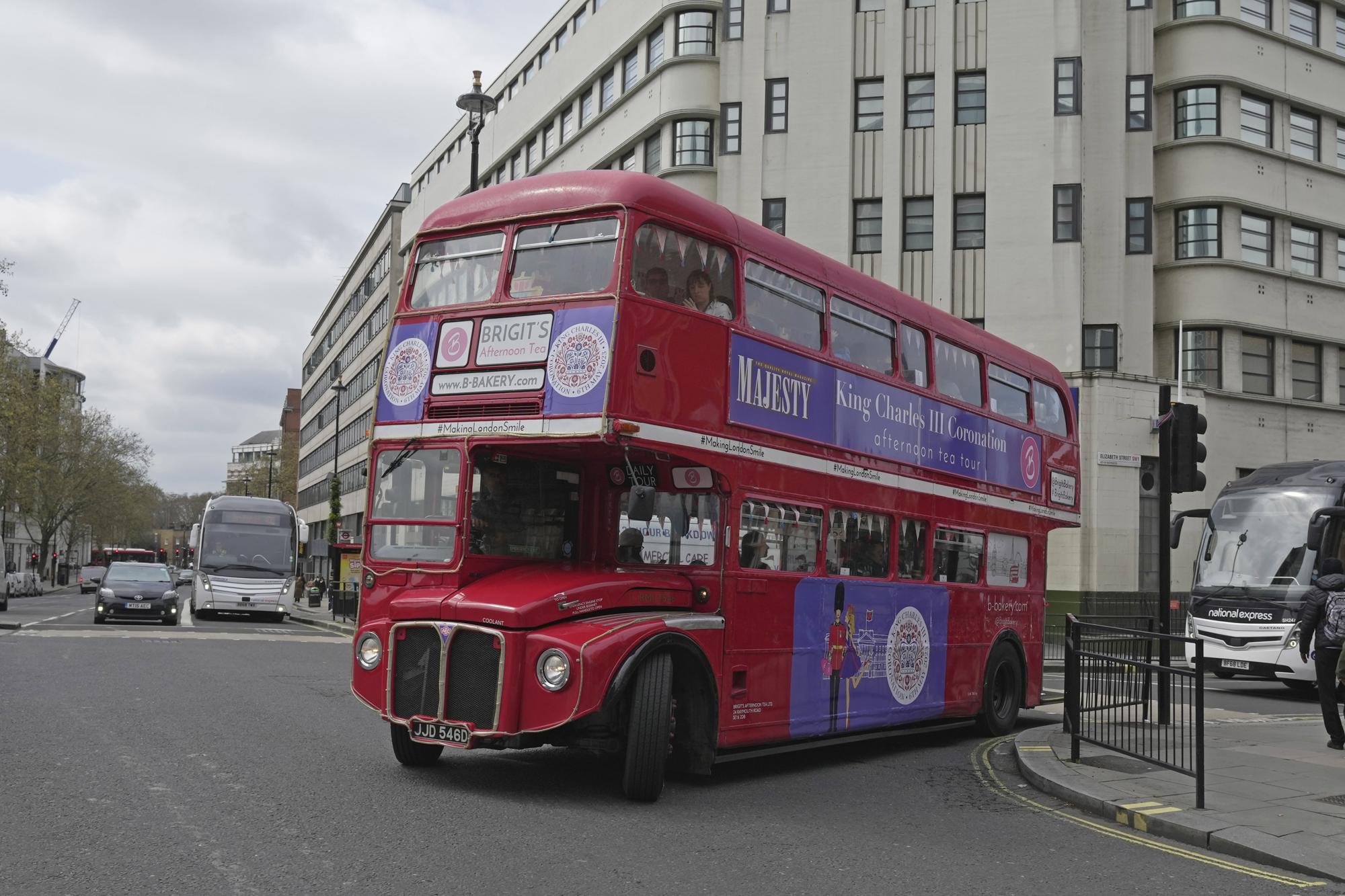 A Coronation Tour Bus departs from Victoria coach station, in London, Monday, April 24, 2023. The May 6 coronation is luring royal fans and far-flung visitors fascinated by the ceremonial spectacle — and drama — of the monarchy and eager to experience a piece of British history. Tour companies, shops and restaurants are rolling out the red carpet, whether it's a decked-out bus tour of London's top sights boasting high tea or merchandise running from regal to kitschy. (AP Photo/Kin Cheung)