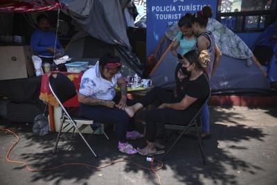 La migrante hondureña Valentina García, izquierda, le hace un pedicure a Elena Cruz, una migrante de El Salvador, el jueves 1 de julio de 2021 en un campamento de migrantes cerca del puente fronterizo peatonal El Chaparral, en Tijuana, México. (AP Foto/Emilio Espejel)