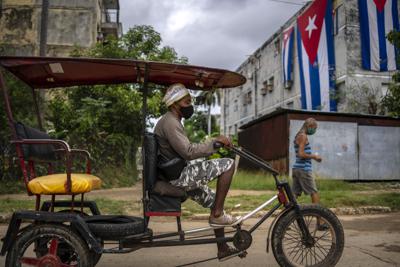 Un taxi bicicleta pasa por la casa de Yunior García, uno de los organizadores de una marcha opositora prohibida, envuelta con banderas cubanas como una forma de bloquear sus ventanas e impedirle comunicarse con el exterior en La Habana, Cuba, el lunes 15 de noviembre de 2021. (AP Foto/Ramón Espinosa)