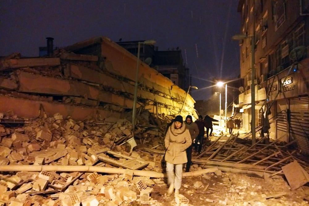 Personas caminan junto a edificios destruidos por un terremoto en Malatya, Turquía, el lunes 6 de febrero de 2023. Un poderoso sismo derribó varios edificios en el sureste de Turquía y Siria y se temen muchas víctimas.  (Imágenes DIA vía AP)