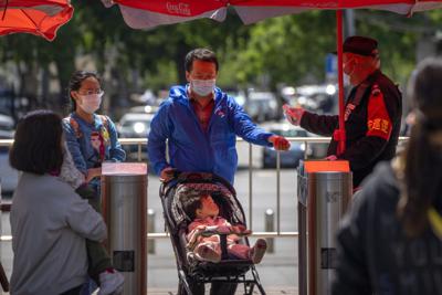 Un guardia de seguridad toma la temperatura de visitantes que entran a un parque público en Beijing el 30 de abril del 2022.   (AP Foto/Mark Schiefelbein)