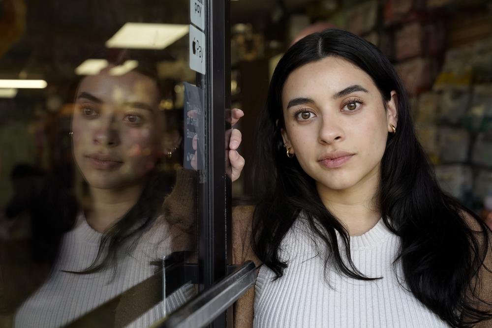 Karla Morales, of Revere, Mass., stands for a photograph at an entrance to her families' party supply shop, in the East Boston neighborhood of Boston, Sunday, March 27, 2022. Morales, who left El Salvador with her family when she was 3 years old, and has been on Temporary Protected Status, or TPS, nearly her whole life, says the status has allowed her family to work, build a successful small business and pay taxes but without providing a pathway to citizenship. (AP Photo/Steven Senne)