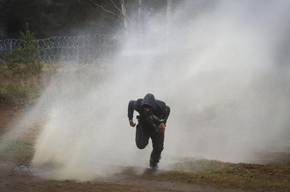 Un hombre huye de un cañón hidrante durante choques entre migrantes y agentes fronterizos polacos en la frontera polaco-bielorrusa cerca de Grodno, Bielorrusia, martes 16 de noviembre de 2021. (Leonid Shcheglov/BelTA via AP)
