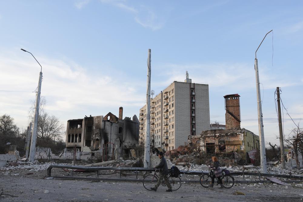 Personas caminan con bicicletas frente a edificios de apartamentos destruidos por bombardeos en Chernihiv, Ucrania, el jueves 7 de abril de 2022. (Foto AP/Evgeniy Maloletka)