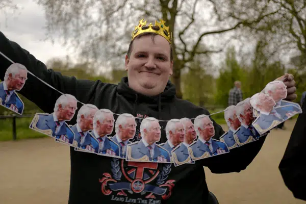Un entusiasta de la realeza lleva una corona mientras sostiene decoraciones que representan al rey Carlos III de Gran Bretaña, mientras acampa a lo largo del Mall, una semana antes de su coronación, en Londres, el domingo 30 de abril de 2023. (AP Foto/Alberto Pezzali)