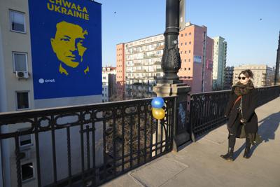 Una mujer pasa por delante de una imagen del presidente de Ucrania, Volodymyr Zelenskyy, en un edificio y globos con los colores de la bandera ucraniana atados al puente Poniatowski en Varsovia, Polonia, el sábado 19 de marzo de 2022. (AP Foto/Czarek Sokolowski)