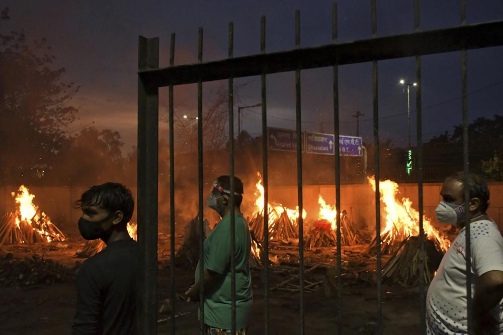 FILE - In this May 6, 2021, file photo, people watch burning funeral pyres of their relatives who died of COVID-19 in a ground that has been converted into a crematorium in New Delhi, India. Indias excess deaths during the pandemic could be a staggering 10 times the official COVID-19 toll, likely making it modern Indias worst human tragedy, according to the most comprehensive research yet on the ravages of the virus in the south Asian country. (AP Photo/Ishant Chauhan, File)