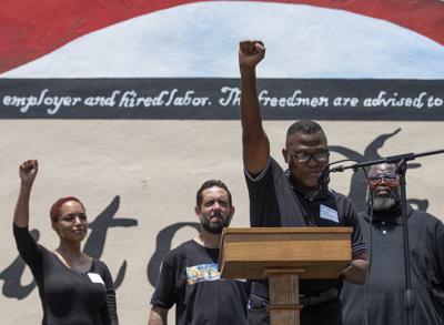 Samson Adenugba levanta su puño durante la ceremonia de dedicación del mural "Igualdad absoluta", parte del Proyecto Legado Juneteenth, el sábado 19 de junio de 2021 en Galveston, Texas. (Godofredo A. Vásquez/Houston Chronicle vía AP)