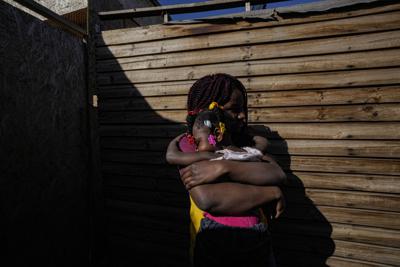 Develine, nacida en República Dominicana de padres haitianos, sostiene a su hermana Cataleya, nacida en Chile, de dos años, afuera de su casa donde viven con su madre Magdaline Afred, quien tiene residencia permanente en Chile, en el campamento "Dignidad" de Santiago establecido por migrantes en Chile, el jueves 30 de septiembre de 2021.  (AP Foto/Esteban Felix)