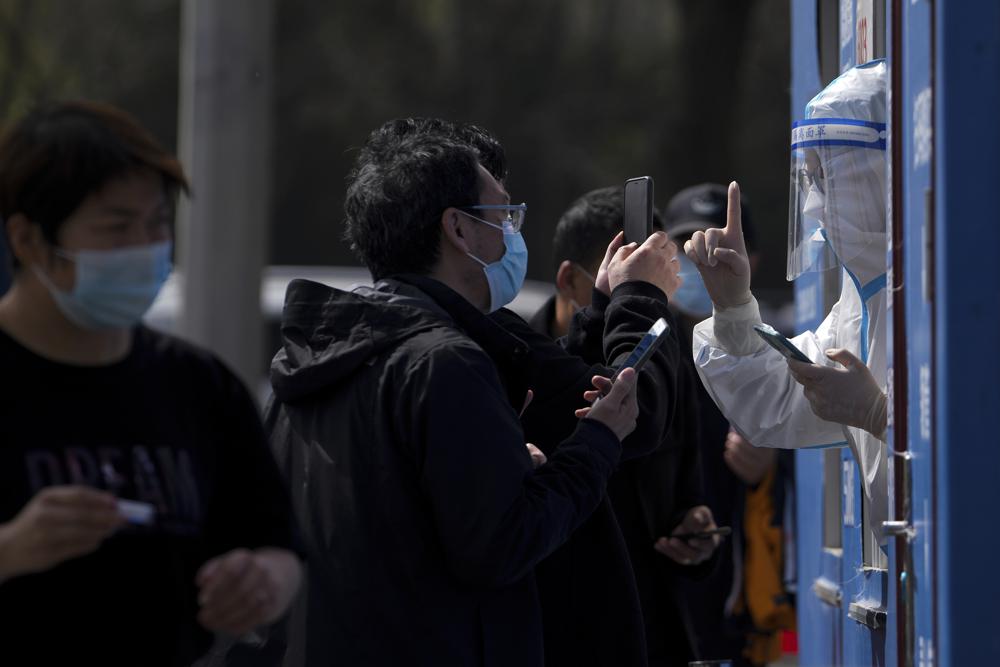 Residents wearing face masks to help protect from the coronavirus talk to a health worker and they line up to get their throat swab at a coronavirus testing site, Tuesday, April 5, 2022, in Beijing. China has sent more than 10,000 health workers from across the country to Shanghai, including 2,000 military medical staff, as it struggles to stamp out a rapidly spreading COVID-19 outbreak in China's largest city. (AP Photo/Andy Wong)