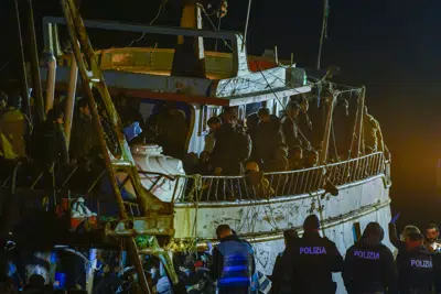 Varios policías, abajo, aguardan frente a un barco pesquero con unos 500 migrantes la madrugada del sábado 11 de marzo de 2023 en el puerto de Crotone, en el sur de Italia. (AP Foto/Valeria Ferraro)