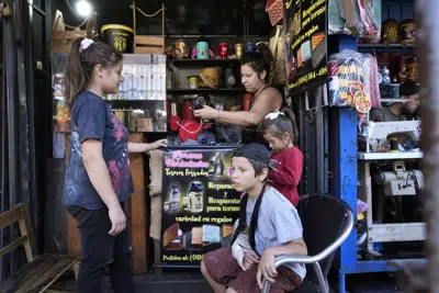 Lorena Ocampos, arriba a la derecha, trabaja en su tienda de termos en el Mercado #4 en Asunción, Paraguay, el sábado 22 de abril de 2023. La madre soltera de 35 años está acompañada por tres de sus cuatro hijos, Gabina, a la izquierda, Calvin, abajo, y Abigail. Las elecciones generales de Paraguay están programadas para el 30 de abril. (AP Foto/Jorge Saenz)