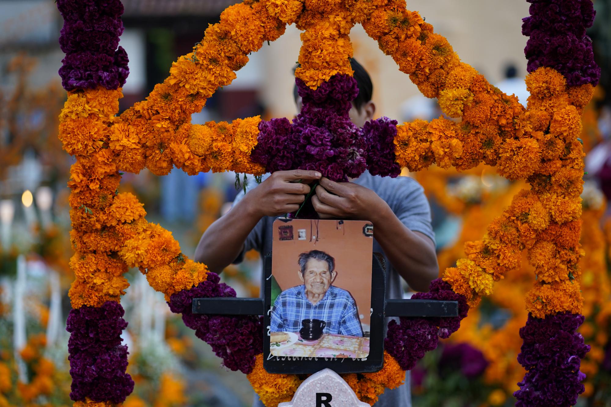 A relative builds an altar as he prepares to spend the night next to the tomb of his loved one during Day of the Dead festivities at the the Arocutin cemetery in Michoacan state, Mexico, Monday, Nov. 1, 2021. In a tradition that coincides with All Saints Day and All Souls Day, families decorate the graves of departed relatives with flowers and candles, and spend the night in the cemetery, eating and drinking as they keep company with their deceased loved ones. (AP Photo/Eduardo Verdugo)