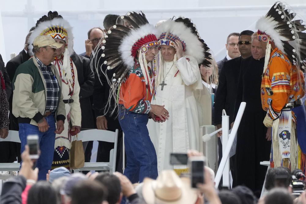 Pope Francis puts on an indigenous headdress during a meeting with indigenous communities, including First Nations, Metis and Inuit, at Our Lady of Seven Sorrows Catholic Church in Maskwacis, near Edmonton, Canada, Monday, July 25, 2022. Pope Francis begins a "penitential" visit to Canada to beg forgiveness from survivors of the country's residential schools, where Catholic missionaries contributed to the "cultural genocide" of generations of Indigenous children by trying to stamp out their languages, cultures and traditions. Francis set to visit the cemetery at the former residential school in Maskwacis. (AP Photo/Gregorio Borgia)