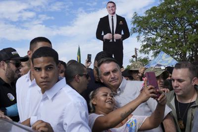 El presidente de Brasil, Jair Bolsonaro (centro), se toma una fotografía con una seguidora mientras hace campaña para su reelección en un asentamiento de trabajadores rurales en Nova Jerusalem, en Brasilia, Brasil, el 24 de octubre de 2022. Bolsonaro se medirá al expresidente Luiz Inácio Lula da Silva en el balotaje previsto para el 30 de octubre. (AP Foto/Eraldo Peres)