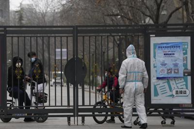 Los residentes de una comunidad cerrada miran desde una puerta cerrada mientras un trabajador con equipo de protección monitorea el acceso el domingo 13 de marzo de 2022 en Beijing. El número de nuevos casos de coronavirus en un brote en el noreste de China se triplicó el domingo y las autoridades reforzaron el control sobre el acceso a Shanghai en el este, suspendiendo el servicio de autobuses a la ciudad de 24 millones de habitantes y requiriendo una prueba de virus para cualquier persona que quiera ingresar. (AP Foto/Ng Han Guan)