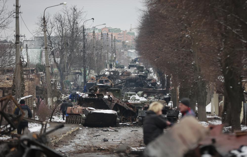 People look at the gutted remains of Russian military vehicles on a road in the town of Bucha, close to the capital Kyiv, Ukraine, Tuesday, March 1, 2022. Russia on Tuesday stepped up shelling of Kharkiv, Ukraine's second-largest city, pounding civilian targets there. Casualties mounted and reports emerged that more than 70 Ukrainian soldiers were killed after Russian artillery recently hit a military base in Okhtyrka, a city between Kharkiv and Kyiv, the capital. (AP Photo/Serhii Nuzhnenko)