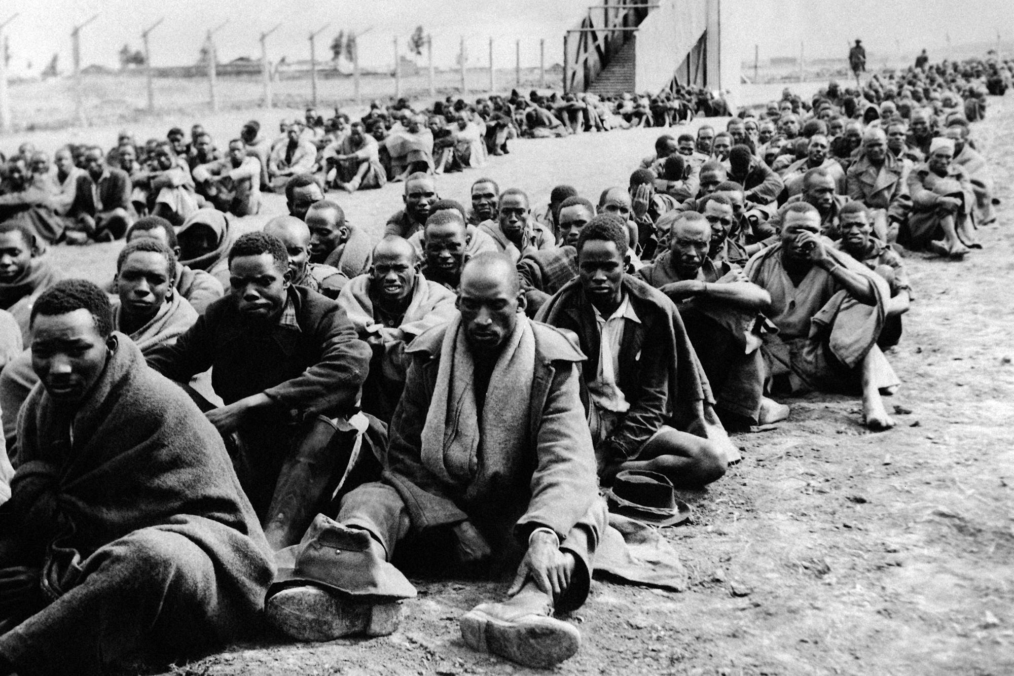 Some of the many Kikuyu tribesmen who were detained as Mau Mau suspects after the forced evacuation of Kikuyus accused of squatting on European farms in the Thomson's Falls area, Kenya, wait to be transported on Nov. 30, 1952. The enclosure is surrounded by barbed wire. The tall structure seen in center background is one of the portable gallows brought from Nairobi for hangings. (AP Photo, File)