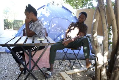 Los cameruneses Daniel Ejube (der) y Enjei Grace hacen tiempo sentados en una mesa junto a la carpa de las Naciones Unidas donde viven en la zona de seguridad que separta el norte del sur en Chipre. Llevan cinco meses viviendo allí, a la espera de que se resuelva su situación.El sur se niega a admitirlos y que puedan tramitar un pedido de asilo. El norte los devolvería a Camerún. (AP Photo/Philippos Christou)