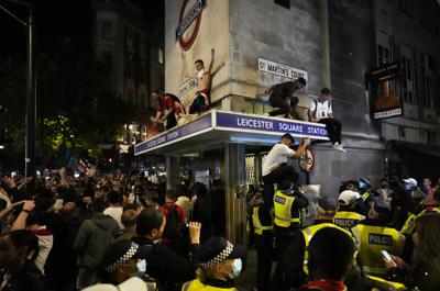 Aficionados ingleses celebran sobre el cartel de la estación de metro de Leicester Square tras la victoria de la selección inglesa de fútbol en su partido de semifinales contra Dinamarca en la Euro 2020, disputado en el estadio Wembley de Londres, el miércoles 7 de julio de 2021. (AP Foto/Matt Dunham)
