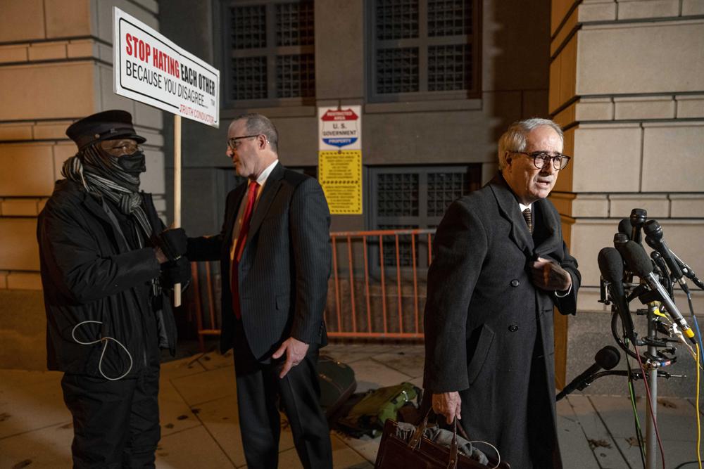 A man holding a sign that reads "Stop Hating Each Other Because You Disagree" refuses to move from behind The attorneys for Oath Keepers leader Stewart Rhodes Edward Tarpley, right, and James Lee Bright, center, as they speak to members of the media outside the Federal Courthouse following a verdict in the Stewart Rhodes trial in Washington, Tuesday, Nov. 29, 2022. Rhodes was convicted of seditious conspiracy for a violent plot to overturn Democrat Joe Biden's presidential win, handing the Justice Department a major victory in its massive prosecution of the Jan. 6, 2021, insurrection. (AP Photo/Andrew Harnik)