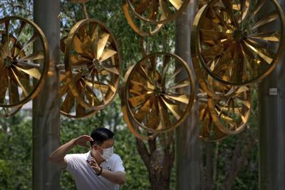 Un hombre con mascarilla contra los contagios de coronavirus hace ejercicio cerca de una instalación con ventiladores en un parque público en Beijing, el martes 15 de junio de 2021. (AP Foto/Andy Wong)