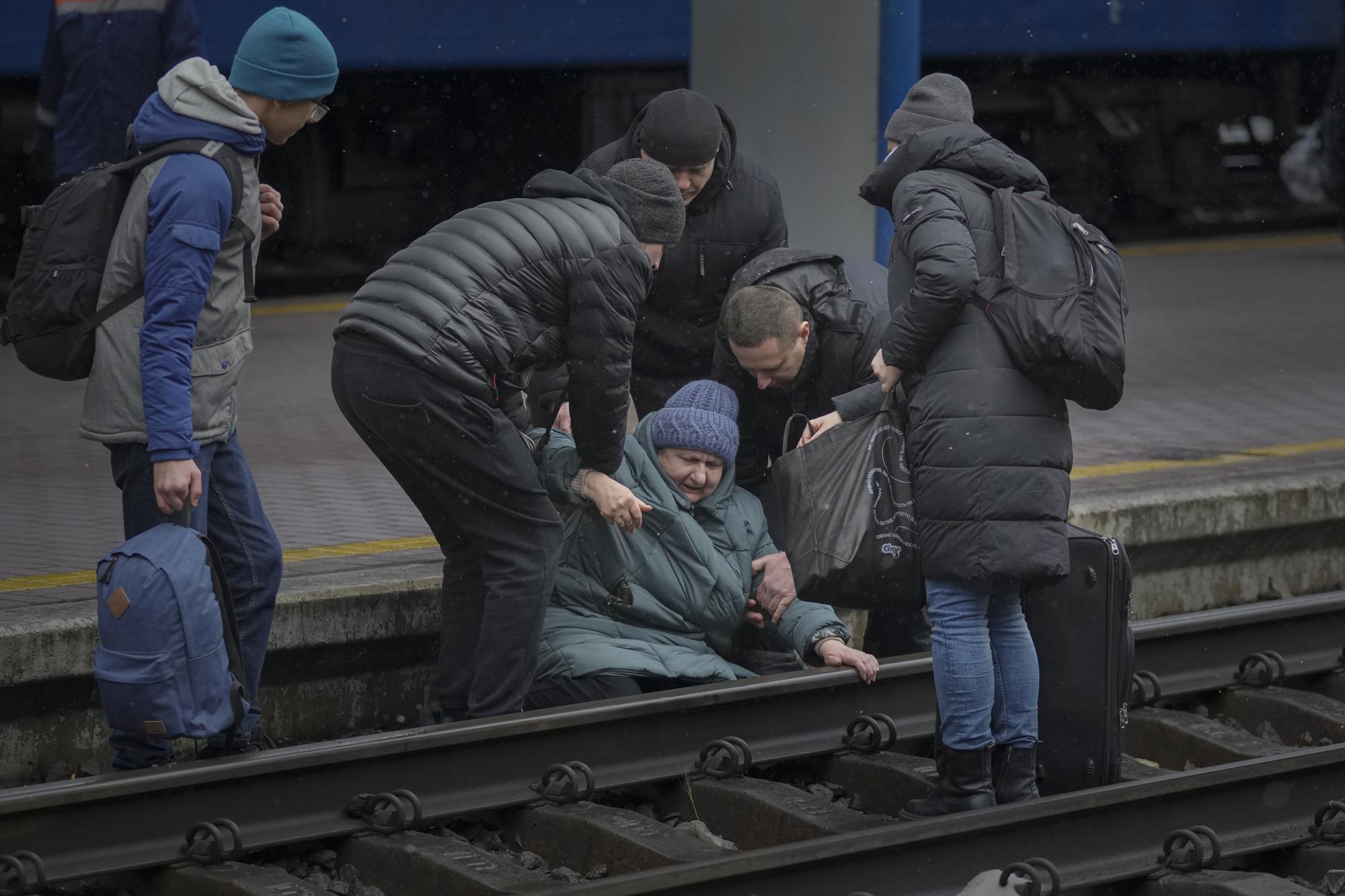 A woman gets help after falling on the tracks trying to reach a Lviv bound train, in Kyiv, Ukraine, Thursday, March 3, 2022. (AP Photo/Vadim Ghirda)