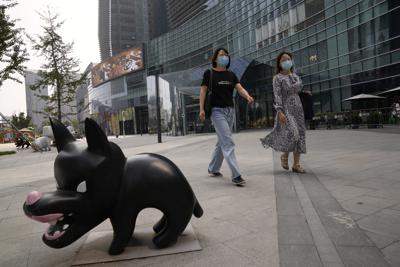 Mujeres que llevan mascarillas debido al coronavirus pasan cerca de la escultura de un perro en Beijing, China, el viernes 10 de septiembre de , 2021. (AP Foto/Ng Han Guan)