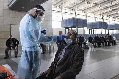 Un médico de Magen David Adom, el servicio nacional de emergencia de Israel, realiza pruebas de COVID-19 en palestinos que ingresan a Israel desde la Franja de Gaza en el cruce de Erez, en la frontera entre Israel y Gaza, el jueves 16 de diciembre de 2021. (Foto AP/Tsafrir Abayov)
