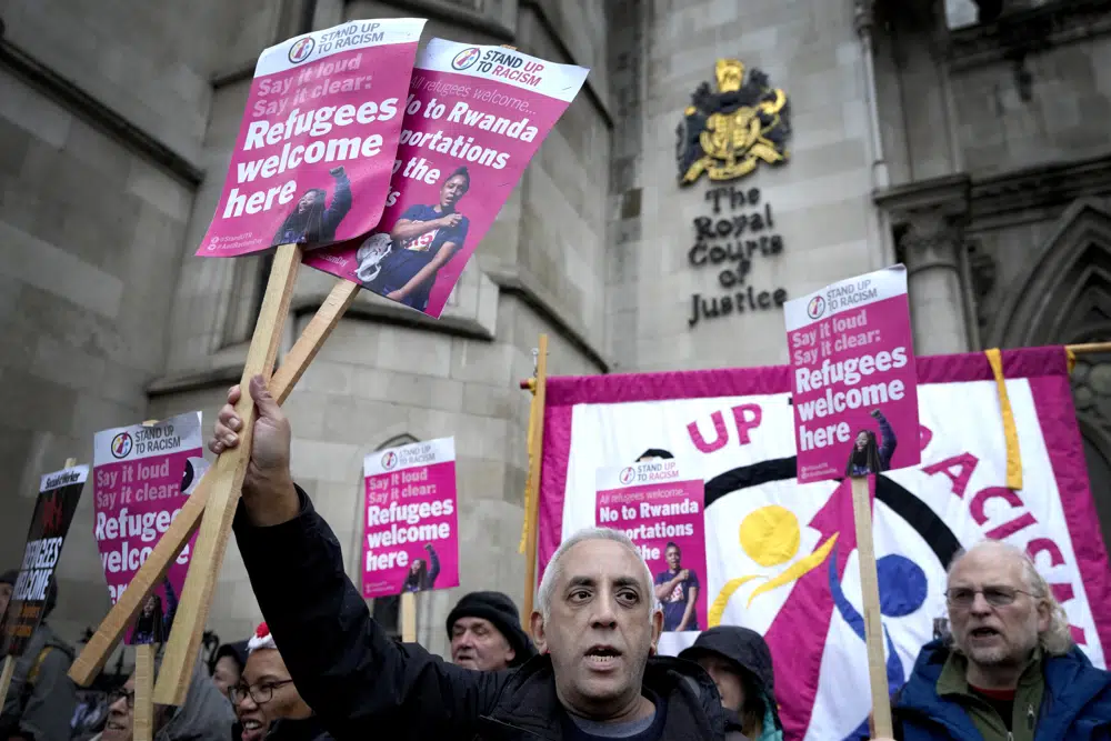 FILE - Stand Up To Racism campaigners hold banners outside the High Court in London, Monday, Dec. 19, 2022. British judges gave the go-ahead Monday, Jan. 16, 2023 for the Court of Appeal to consider challenges to the British government’s plan to send some asylum-seekers on a one-way trip to Rwanda. Two High Court judges ruled in December that the controversial policy is legal, rejecting a lawsuit from several asylum-seekers, aid groups and a border officials’ union. (AP Photo/Kirsty Wigglesworth, File)