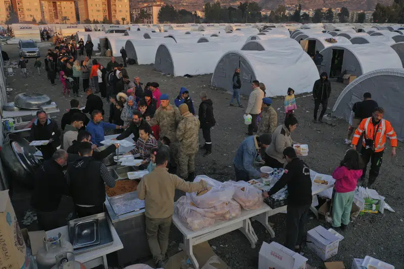Yıkıcı depremde evlerini kaybeden insanlar, 14 Şubat 2023 Salı, İskenderun'daki derme çatma bir kampta yiyecek almak için sıraya giriyor. Bir hafta önce Türkiye ve Suriye'yi vuran büyük depremle binlerce kişi evsiz kaldı. Hayatta kalanları umutsuzca arama çalışmaları muhtemelen son saatlerine girerken, kalabalık çadırlara tıkıldılar veya sıcak yemek için sokaklarda sıraya girdiler.  (AP Fotoğrafı/Hüseyin Malla)