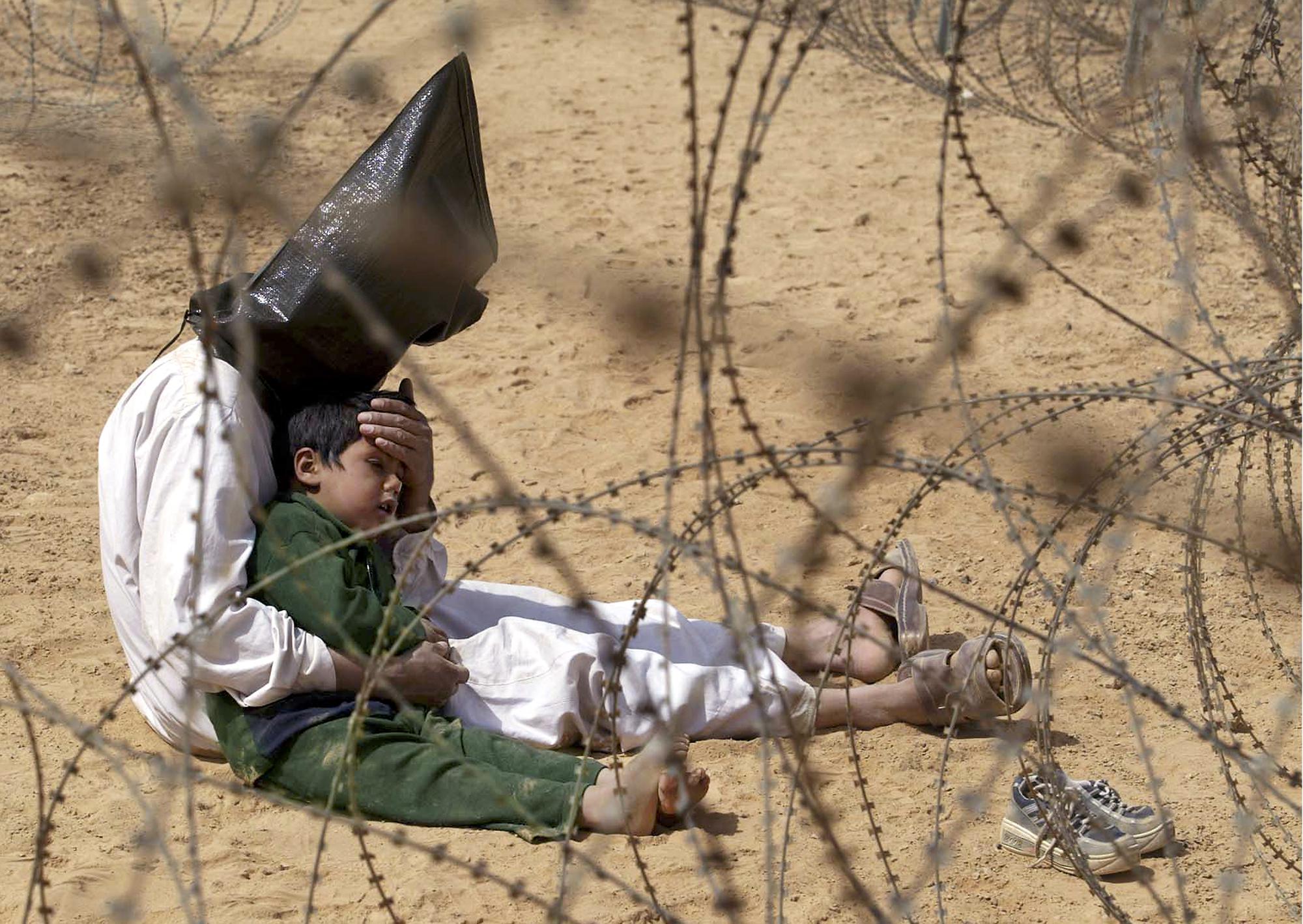 FILE - An Iraqi prisoner of war comforts his 4-year-old son at a regroupment center for POWs of the 101st Airborne Division near An Najaf, Afghanistan, March 31, 2003. The man was seized in An Najaf with his son and the U.S. military did not want to separate father and son. (AP Photo/Jean-Marc Bouju, File)