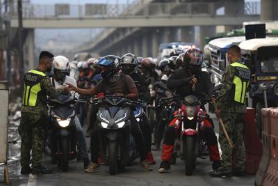 Policías con equipo de protección contra el coronavirus revisan a motociclistas en un retén de salud instalado como precaución contra la propagación del COVID-19 en las afueras de la ciudad de Marikina, Filipinas, el viernes 6 de agosto de 2021. (AP Foto/Basilio Sepe)