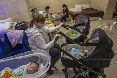Niñeras cuidando de bebés recién nacidos en un sótano convertido en una guardería en Kiev, Ucrania, el sábado 19 de marzo de 2022. Dos decenas de bebés nacidos de madres sustitutas esperan a que sus padres extranjeros puedan viajar al país devastado por la guerra y los lleven a casa. (AP Foto/Rodrigo Abd)