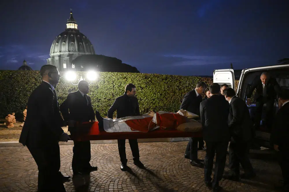 In this image released on Monday, Jan. 2, 2023, by the Vatican Media news service, the body of late Pope Emeritus Benedict XVI is carried from the chapel of the monastery 'Mater Ecclesiae' at The Vatican where he mostly lived after retiring on Feb. 28, 2013, to St. Peter's Basilica, background, where he will be lied out in state. Pope Benedict, the German theologian who will be remembered as the first pope in 600 years to resign, has died, the Vatican announced Saturday, Dec. 31, 2022. He was 95. (Vatican Media via AP)