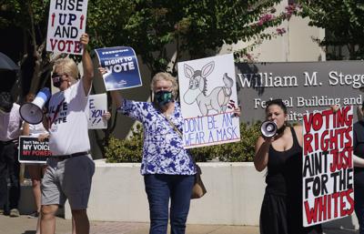 Varios manifestantes protestan fuera del lugar donde el gobernador de Texas, Greg Abbott, promulgó un proyecto de ley del Senado, llamado Bill 1, también conocido como ley de integridad electoral, en Tyler, Texas, el martes 7 de septiembre de 2021. (AP Foto/LM Otero)