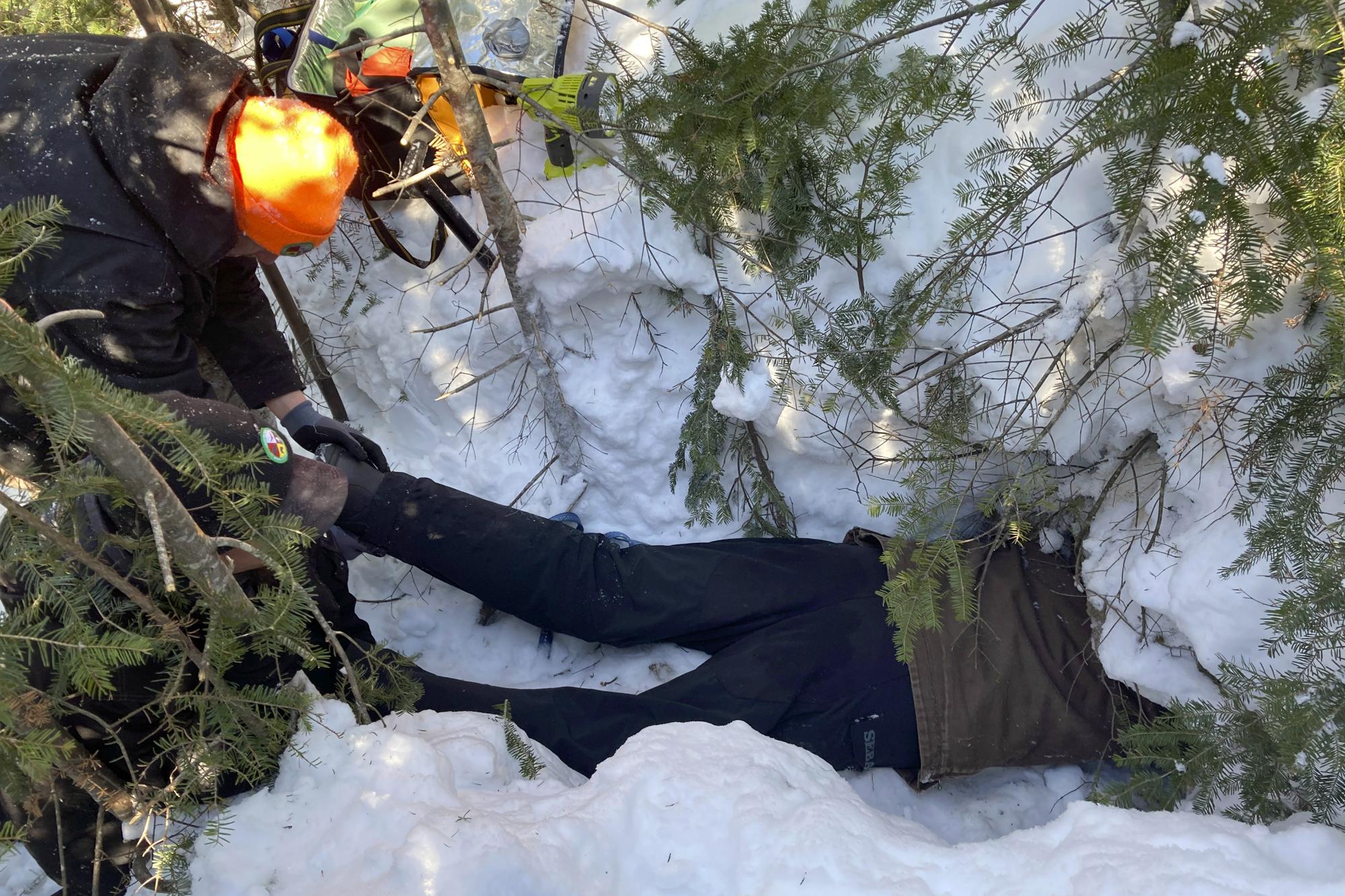 Todd Kautz, a post-doctoral researcher from the State University of New York, lies on his belly to take biological samples from a hibernating bear in its den as a colleague holds his feet in Grand Portage, Minn. on March 2, 2022. This includes testing the young black bear for the coronavirus. (AP Photo/Laura Ungar)