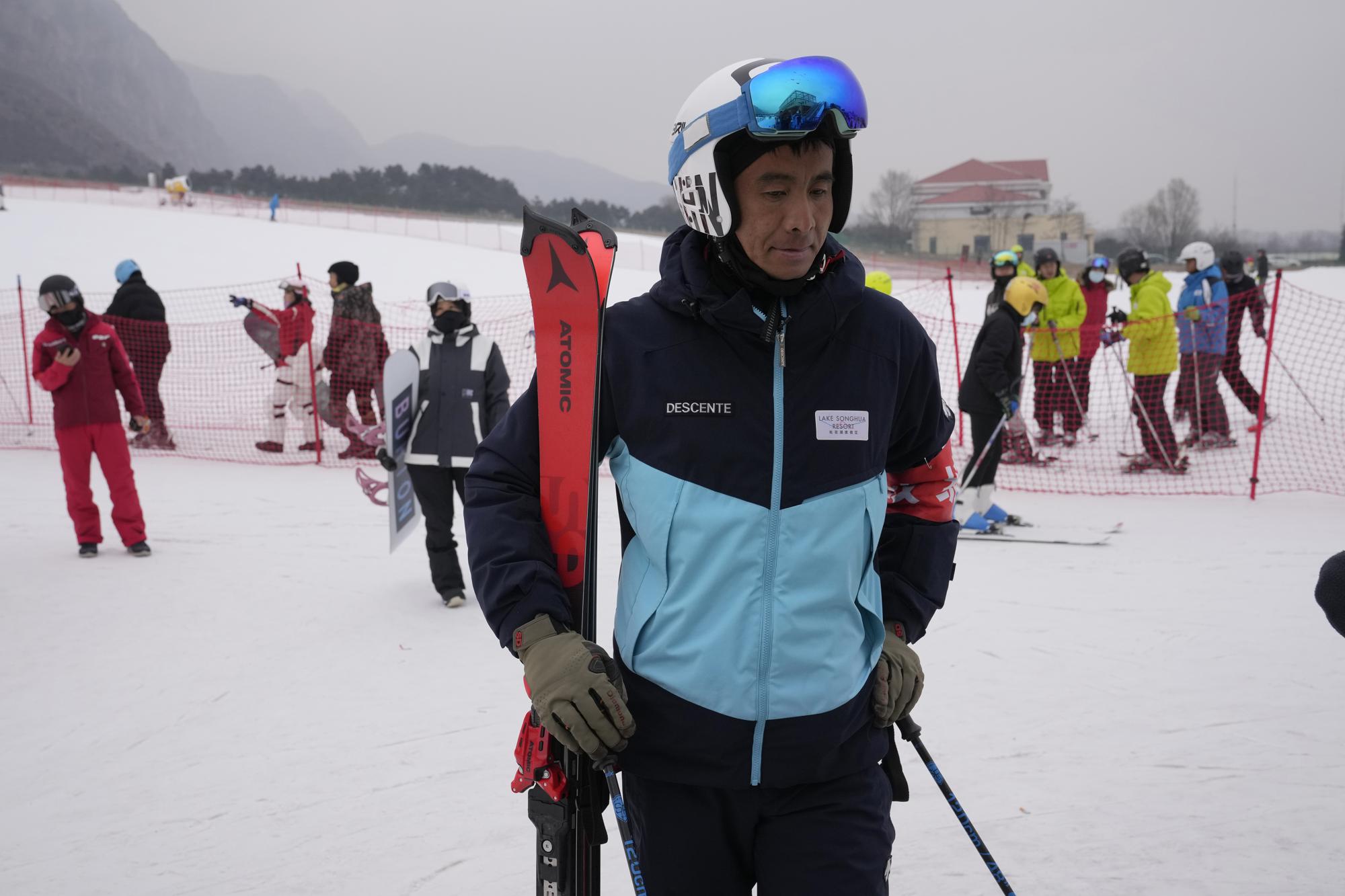 Farmer-turned-ski coach Li Wei looks as ski enthusiasts take to the slope at the Vanke Shijinglong Ski Resort in Yanqing on the outskirts of Beijing, China, Thursday, Dec. 23, 2021. The Beijing Winter Olympics is tapping into and encouraging growing interest among Chinese in skiing, skating, hockey and other previously unfamiliar winter sports. It's also creating new business opportunities. (AP Photo/Ng Han Guan)