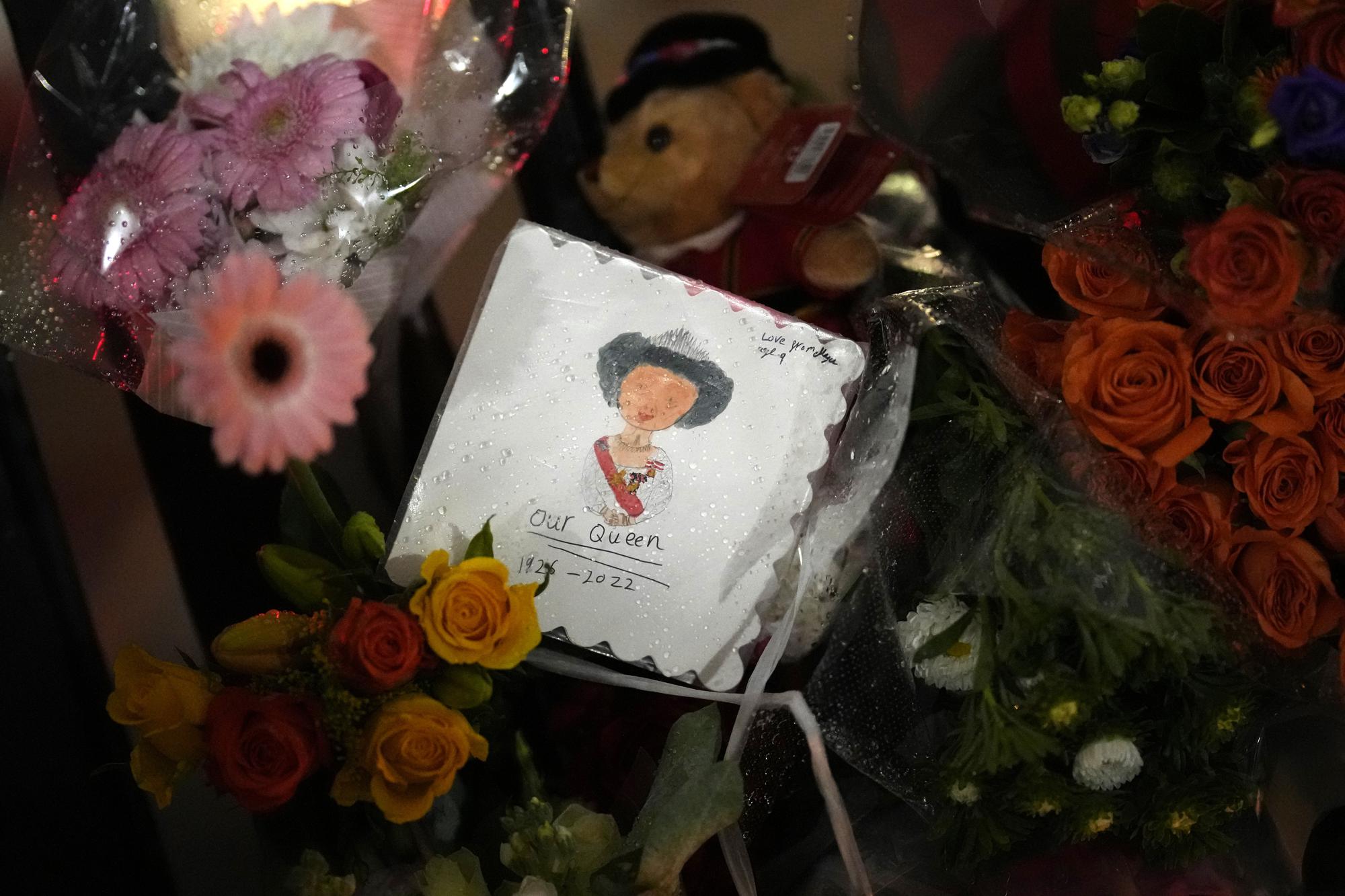A draw of Britain's Queen Elizabeth II is placed with flowers outside Buckingham Palace in London, Friday, Sept. 9, 2022. Queen Elizabeth II, Britain's longest-reigning monarch and a rock of stability across much of a turbulent century, died Thursday after 70 years on the throne. She was 96. (AP Photo/Christophe Ena)