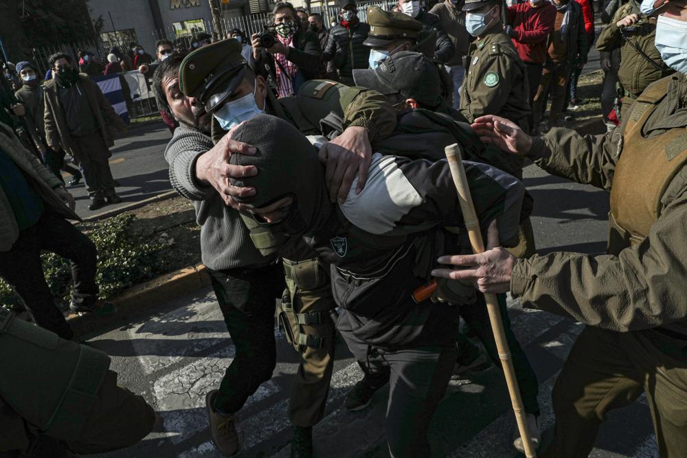 Un partidario del gobierno cubano, detrás a la izquierda, agarra por la cabeza a un manifestante anticubano mientras la policía intenta separarlos frente a la embajada de Cuba en Santiago, Chile, el viernes 16 de julio de 2021. (AP Foto/Esteban Felix)