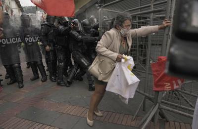 Un policía se prepara para disparar gas lacrimógeno a una manifestante que empuja una verja, la cual fue colocada por la policía con el fin de bloquear el acceso al palacio de gobierno durante protestas contra las políticas económicas de las autoridades, como el incremento mensual a los precios de los combustibles, el miércoles 11 de agosto de 2021, en Quito, Ecuador. (AP Foto/Dolores Ochoa)