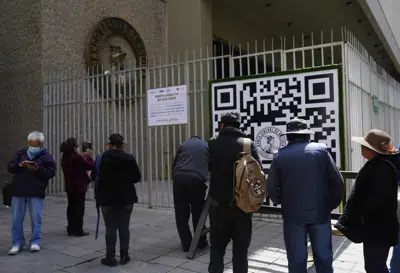 Varias personas miran un código QR afuera del Banco Central de Bolivia que las personas deben usar para registrarse a fin de hacer una cita con el banco que luego le dice al usuario cuántos dólares estadounidenses puede comprar en esa fecha, el martes 11 de abril de 2023 en La Paz, Bolivia. (AP Foto/Juan Karita)