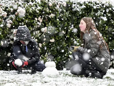 Brody Mielke, de 10 años, a la izquierda, y su hermana mayor, Braelynn, de 12, hacen un muñeco de nieve frente a su casa en Fontana,en la cordillera Hunters, en California, el sábado 25 de febrero de 2023. (Will Lester/The Orange County Register vía AP)