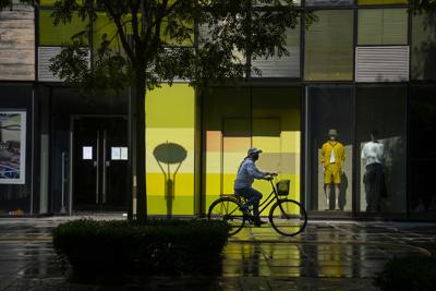 Una mujer, con mascarilla, circula en bicicleta por delante de una tienda cerrada por las medidas contra el COVID-19, en un centro comercial, en Beijing, el 17 de mayo de 2022. (AP Foto/Mark Schiefelbein)