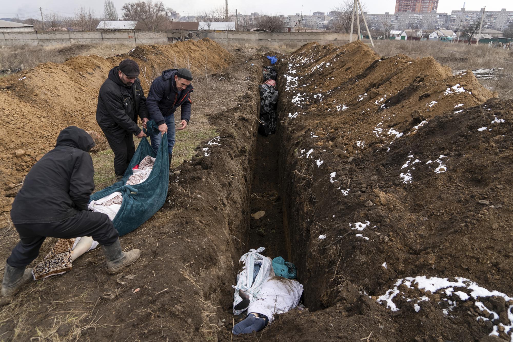 Dead bodies are placed into a mass grave on the outskirts of Mariupol, Ukraine, Wednesday, March 9, 2022, as people cannot bury their dead because of heavy shelling by Russian forces. (AP Photo/Mstyslav Chernov)