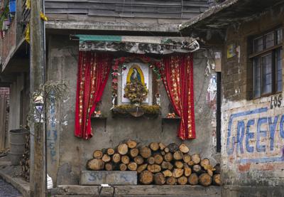 Un altar en honor de la Virgen de Guadalupe decora la fachada de una casa, con la madera para cocinar almacenada debajo, en la comunidad indígena purépecha de Comachuén, en el estado de Michoacán, México, el 19 de enero de 2022. Las remesas de los migrantes en Estados Unidos han permitido que las familias se queden en Comachuén en lugar de irse a otras partes del país en busca de trabajo. (AP Foto/Fernando Llano)