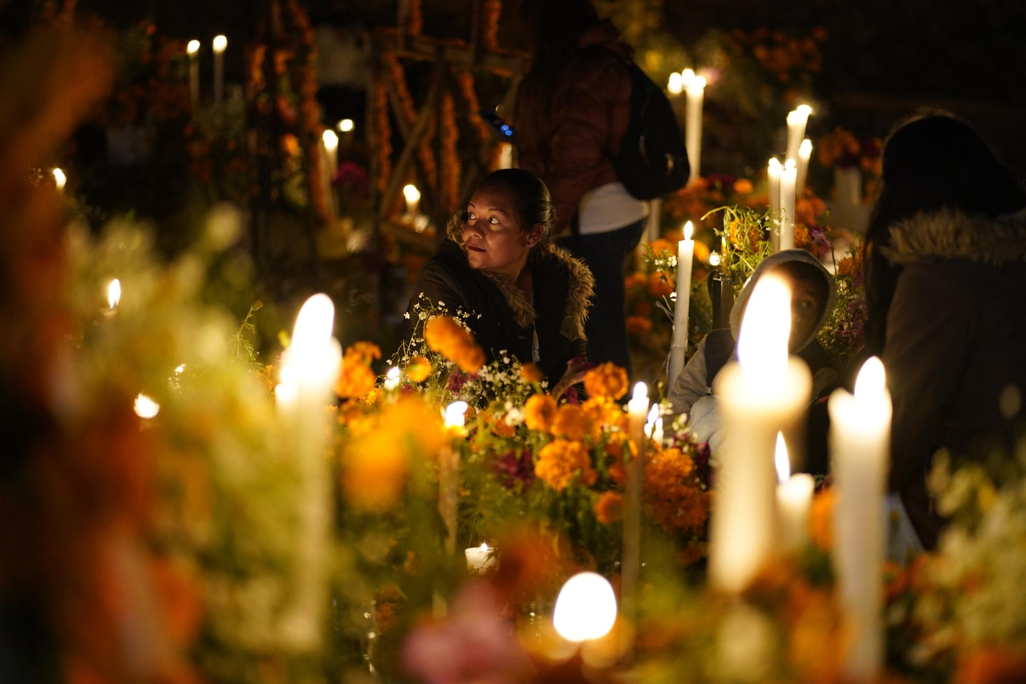 Relatives spend the night next to the tomb of their loved one during Day of the Dead festivities at the the Arocutin cemetery in Michoacan state, Mexico, Monday, Nov. 1, 2021. In a tradition that coincides with All Saints Day and All Souls Day, families decorate the graves of departed relatives with flowers and candles, and spend the night in the cemetery, eating and drinking as they keep company with their deceased loved ones. (AP Photo/Eduardo Verdugo)